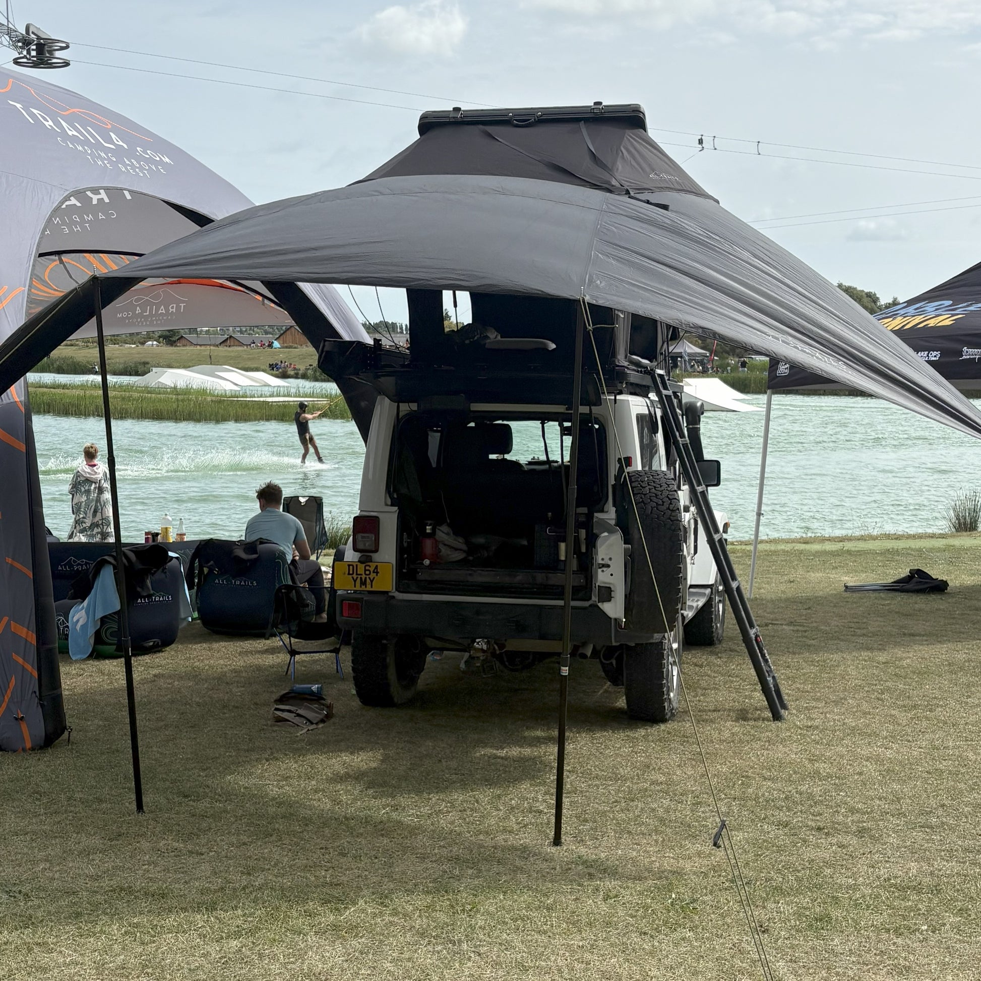 Van with a large canopy set up near a body of water with people in the background.