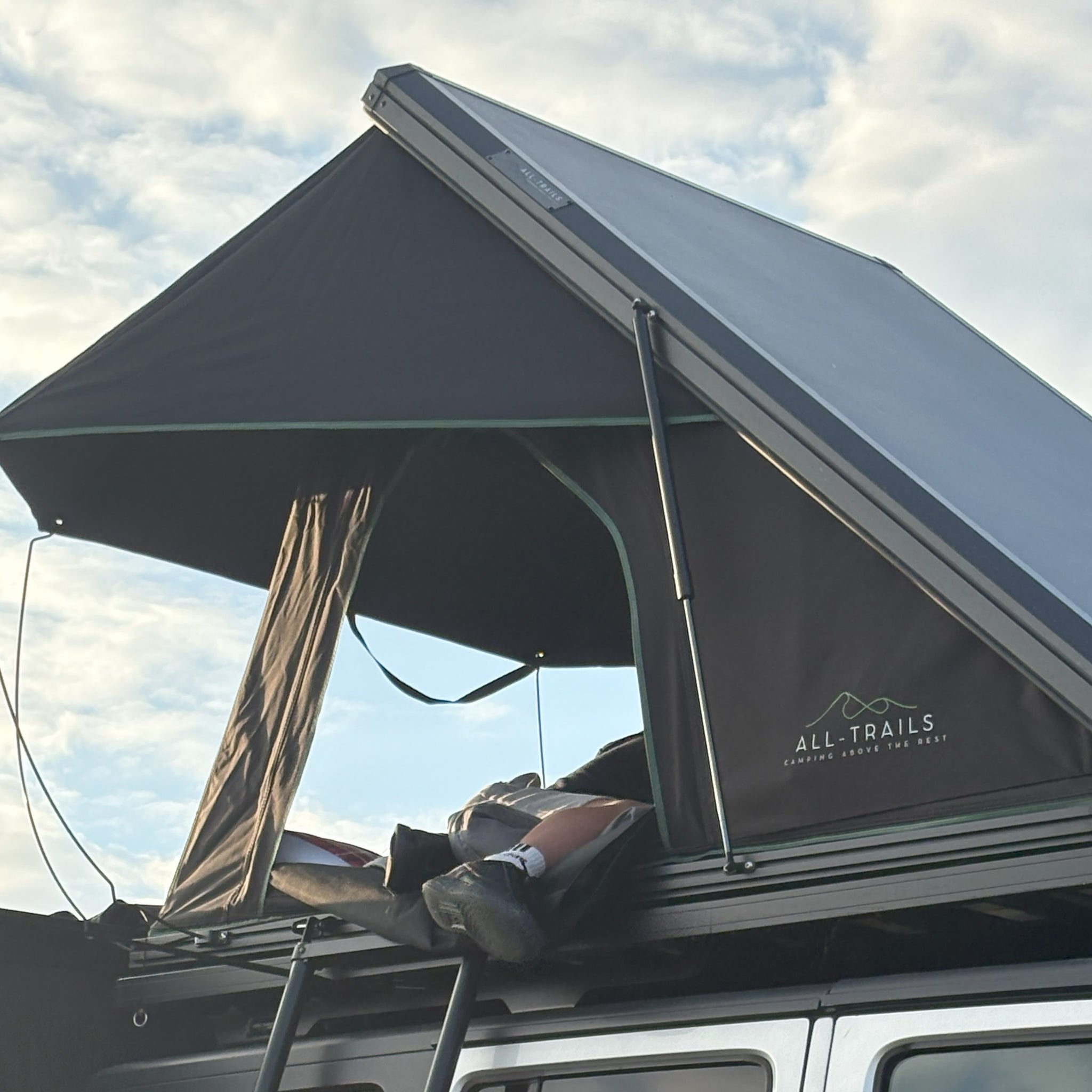 Roof top tent with 'All-Trails' branding from Trail4.com against a cloudy sky