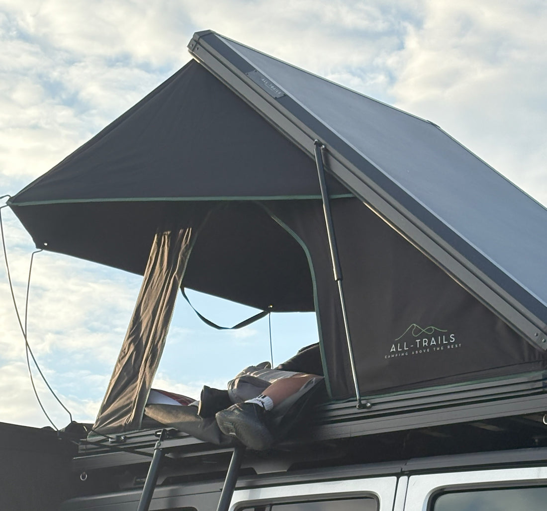 Roof top tent with 'All-Trails' branding from Trail4.com against a cloudy sky