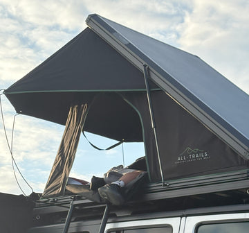 Roof top tent with 'All-Trails' branding from Trail4.com against a cloudy sky