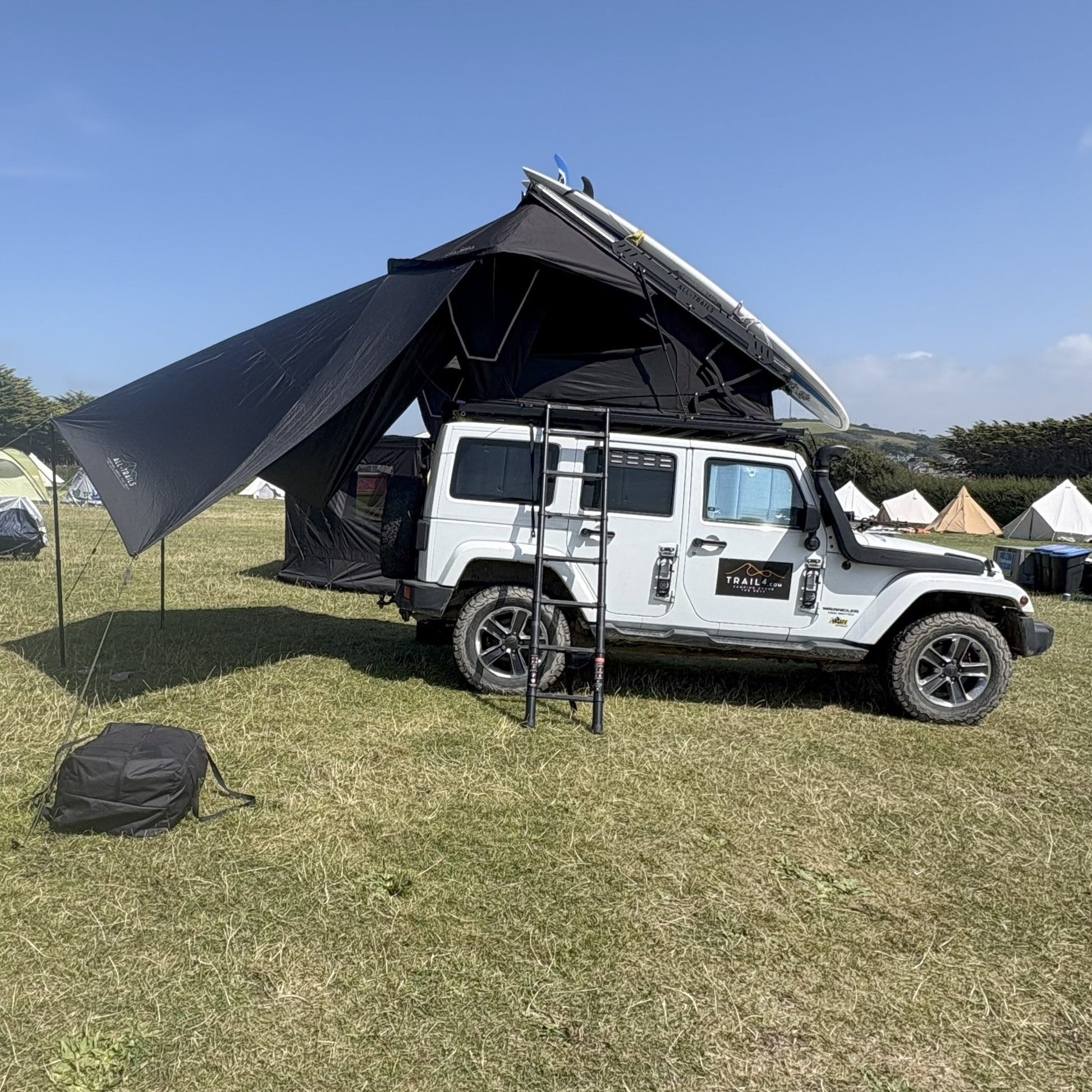 White SUV with a rooftop tent set up on a grassy field under a clear blue sky.